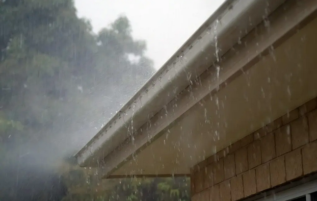 Rainwater overflowing from a residential gutter along a roofline during a heavy rainstorm.