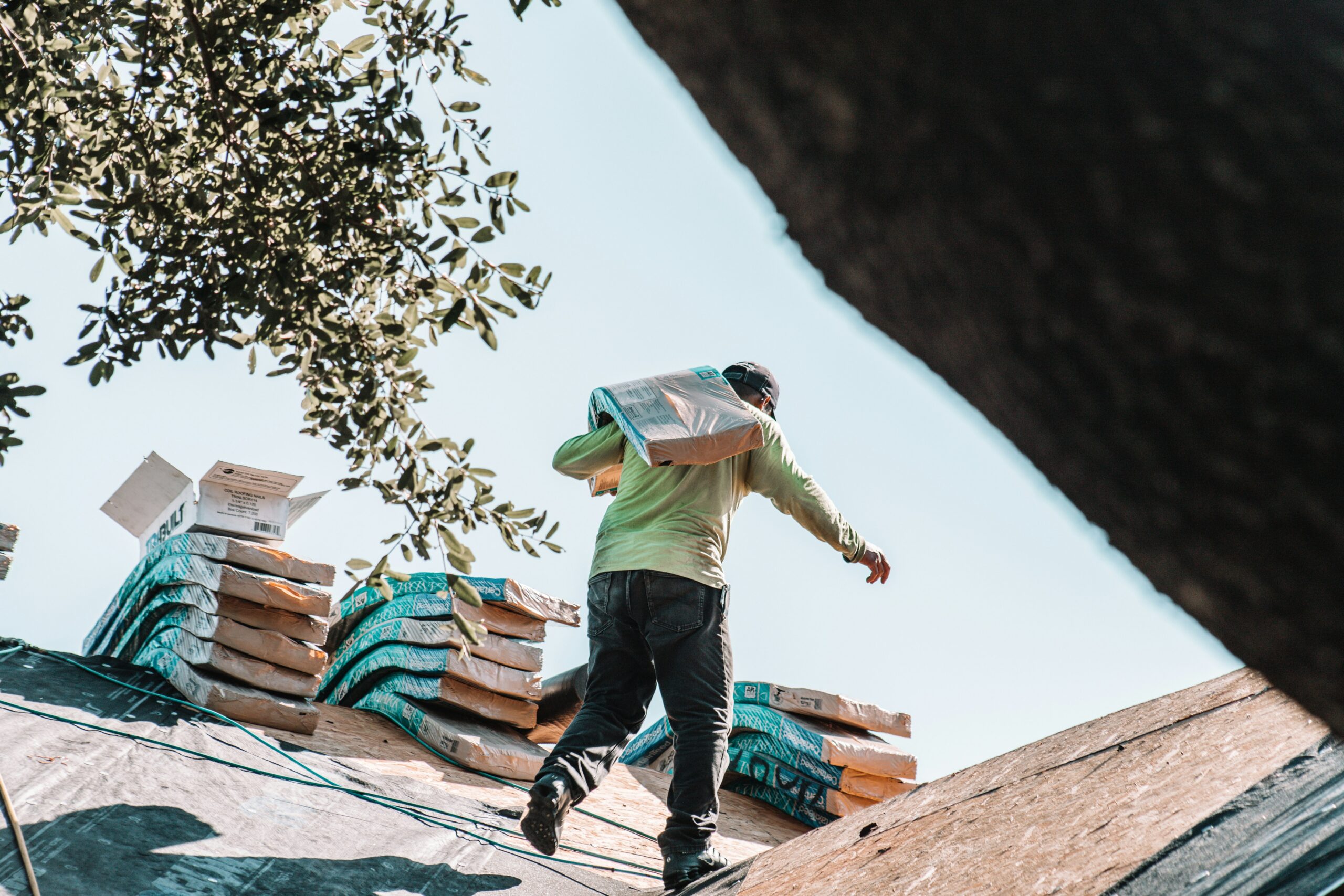 A contractor installing asphalt shingles on a residential roof on a clear spring day.