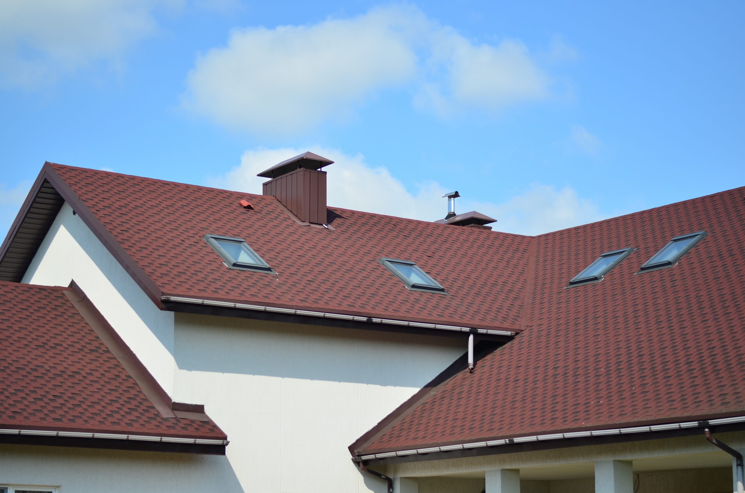 Asphalt shingle roof on a two-story home under a bright summer sky.