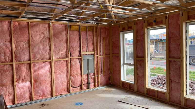Pink batt insulation installed between wooden wall studs in an unfinished room.