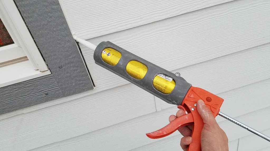A homeowner inspects a cracked caulk seam along exterior siding trim near a window.