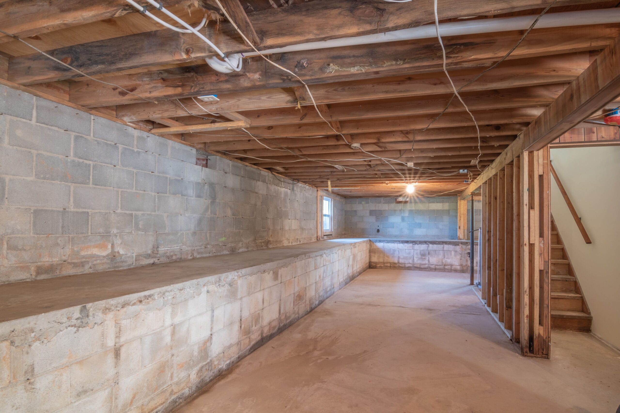 Exposed wood floor joists resting on top of a concrete foundation wall in an unfinished basement ceiling.